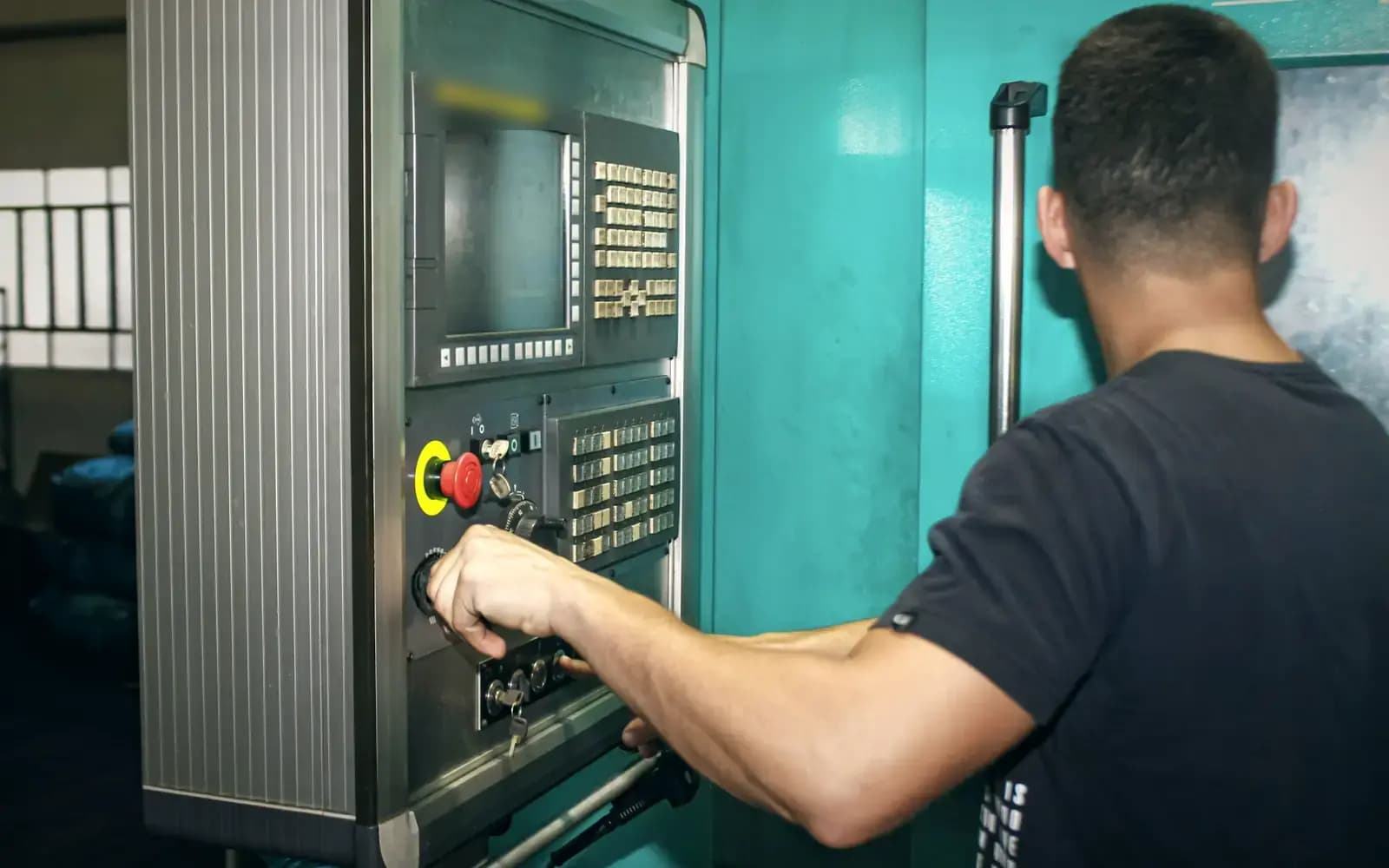 Machinist operating the control panel of a CNC machine on a factory floor