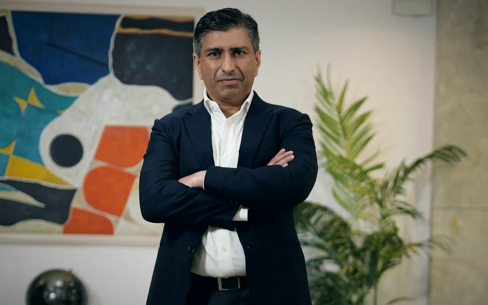 Business executive in a dark suit standing with arms crossed in an office